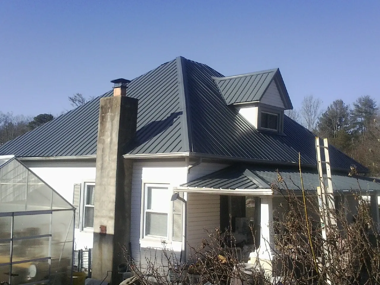 Dark blue standing seam metal roof on a white farmhouse with dormer — Slate & Tile Roof Repair by Roofing Brothers in Pine Meadow