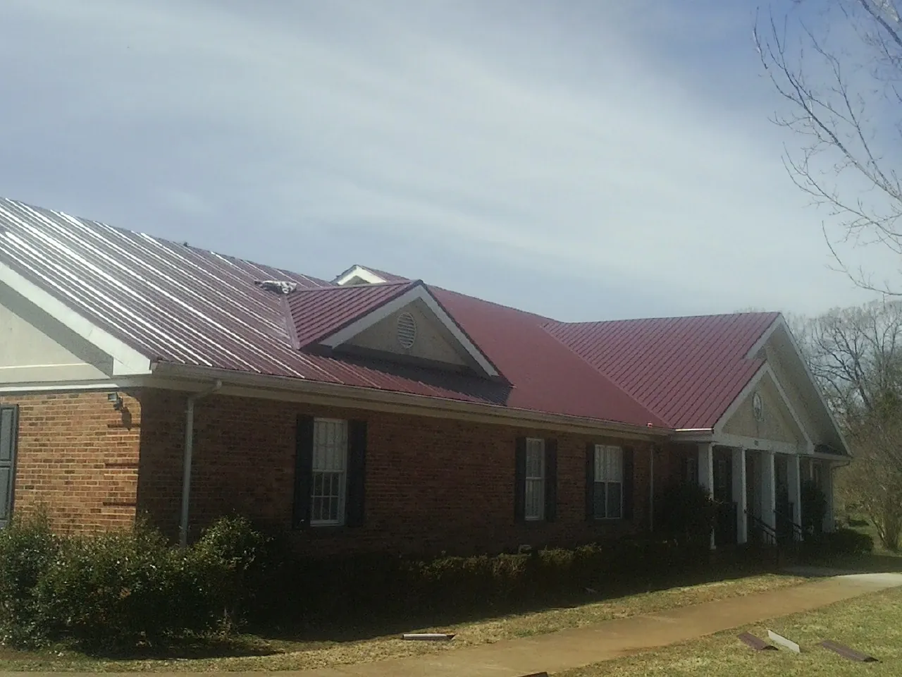 Red metal roof with gabled entries on a long brick building, from a Hail Damage Roof Repair job in Pine Meadow