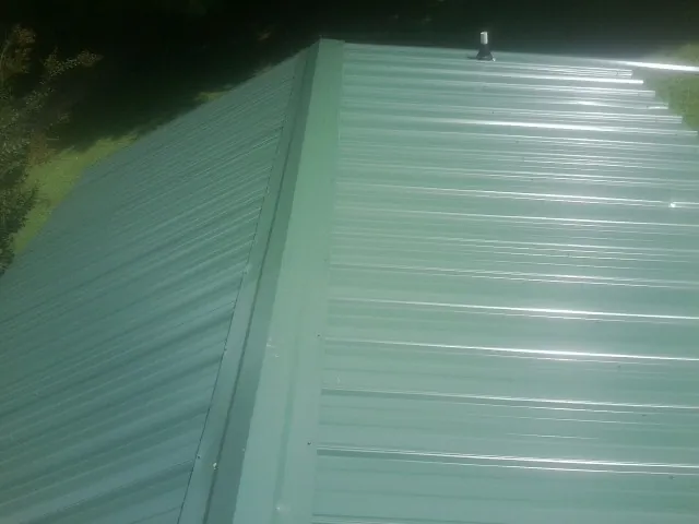 New green metal panels meeting at the ridge of a roof — Flat Roof Repair work by our crew in Pine Meadow